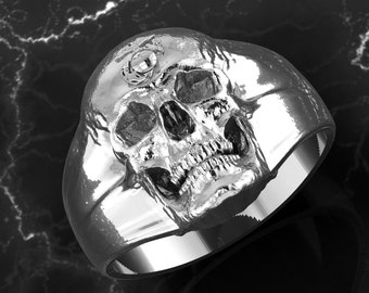 May include: A polished silver skull ring. The ring features a detailed skull design with eye sockets, a nose cavity, and teeth. The band is wide. The ring's design suggests a gothic or biker theme, with a focus on the skull.