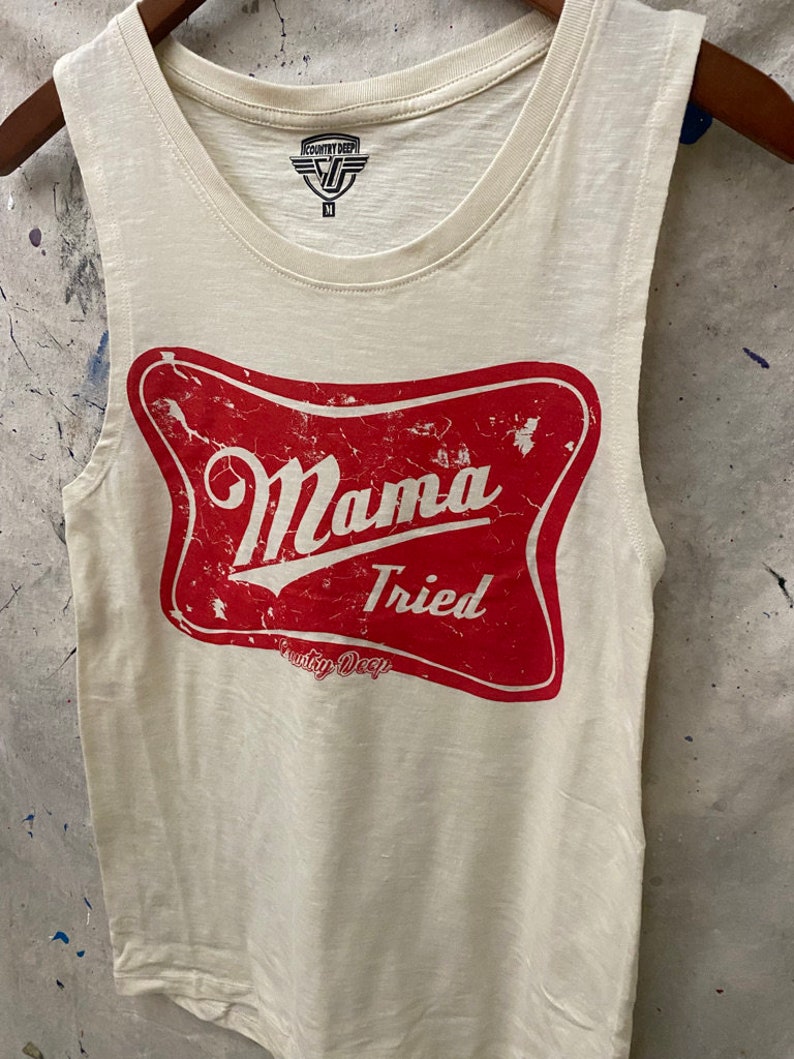 May include: White sleeveless tank top with a red distressed graphic that says "Mama Tried" with the words "Country Deep" underneath. The tank top has a tag that says "Country Deep" with a size "M" on it.
