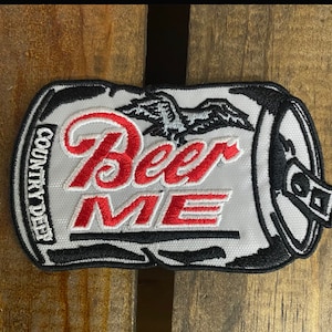 May include: White embroidered patch with a black outline of a beer can. The can has the words "Beer Me" in red and white embroidery. The words "Country Deep" are embroidered on the side of the can.