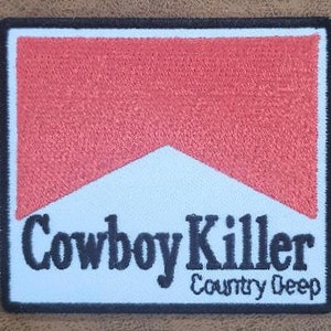 May include: A white patch with a red and white cigarette-style logo and the text "Cowboy Killer Country Deep" in black.