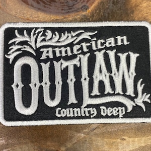 以下が含まれることがあります： 「American Outlaw Country Deep」と白文字で書かれた黒い刺繍パッチ