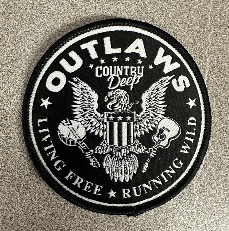 May include: Black and white embroidered patch with an eagle holding a banjo and a guitar. The patch says "Outlaws Country Deep Living Free Running Wild".
