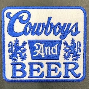 May include: Blue and white embroidered patch with the text "Cowboys And Beer" and two stylized lion figures.