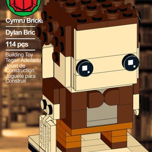 May include: A Lego-style building toy figure, mainly brown and tan, with black details. The figure is on a rectangular base with the name "Dylan Brickas" and the text "Cymru Bricks". The set includes 114 pieces.