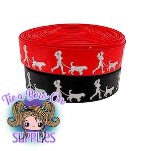 Puede incluir: Dos rollos de cinta, uno rojo y otro negro, están apilados. Cada cinta presenta un patrón repetido de una persona paseando a un perro. La cinta probablemente se utiliza para manualidades o envolver regalos.