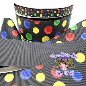 Puede incluir: Una cinta de grosgrain negra con un patrón repetitivo de lunares multicolores en rojo, azul, verde y amarillo. La cinta está enrollada y se muestra con un logotipo que dice Tie a Bow On SUPPLIES junto a una ilustración de un personaje.