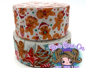 May include: Two rolls of white ribbon with a gingerbread theme. The top roll features gingerbread men and women with red, green, and gold accents. The bottom roll has a festive design with a gingerbread man, Christmas tree, and star.