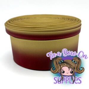 Puede incluir: Un carrete de cinta de grosgrain con un degradado horizontal que transiciona de un rojo burdeos profundo en la parte inferior a un amarillo dorado en la parte superior. La cinta tiene una textura acanalada y está enrollada.