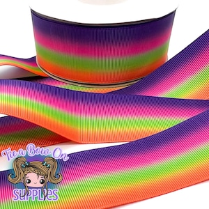 Puede incluir: Un rollo de cinta de grogrén colorida con un degradado arcoíris de morado, rosa, verde y naranja. La cinta está desenrollada, mostrando las vibrantes transiciones de color. El texto "Tie a Bow On SUPPLIES" es visible.