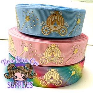 Könnte beinhalten: Drei Rollen Band in Blau, Rosa und Regenbogenfarben. Jedes Band zeigt ein goldenes Kutschen- und Zauberstab-Design. Der Text "Tie a Bow On Supplies" ist auf der unteren Rolle sichtbar.