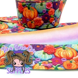 Könnte beinhalten: Eine Rolle dekorativen Bandes mit einem herbstlichen Muster. Das Band zeigt orangefarbene Kürbisse und bunte Blumen auf einem tealfarbenen Hintergrund. Das Band hat auch einen Farbverlauf aus Orange, Rosa und Blau. Der Text "Tie a Bow On SUPPLIES" ist sichtbar.