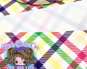 May include: Close-up of a plaid ribbon with a white border. The plaid pattern features yellow, green, red, and purple squares. The image also includes a logo with the text "Tie a Bow On SUPPLIES" and a cartoon girl.