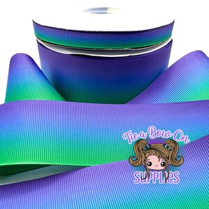 Puede incluir: Un carrete de cinta de grosgrain con un degradado vibrante que va del morado intenso al verde brillante. La cinta tiene una textura acanalada distintiva e incluye un logotipo con el texto Tie a Bow On Supplies y un personaje de dibujos animados.