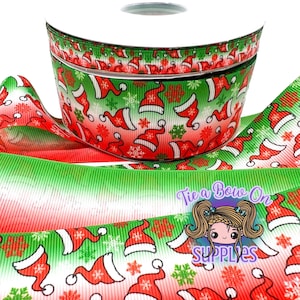 Puede incluir: Un carrete de cinta de grosgrain con un patrón repetitivo de gorros de Papá Noel rojos y blancos y copos de nieve verdes sobre un fondo degradado de rojo a verde. La cinta tiene una superficie texturizada y acanalada e incluye un logotipo.