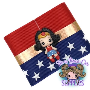 May include: A red, white, and blue ribbon with a gold stripe and white stars, featuring a Wonder Woman figurine. The ribbon is a craft supply, perfect for bows and other DIY projects.