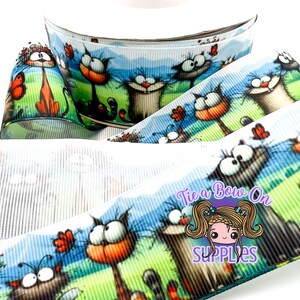 May include: Decorative ribbon featuring a repeating pattern of cartoon cats with exaggerated expressions, set against a backdrop of green grass, blue sky, and butterflies. The ribbon is white with vertical lines and the text "Tie a Bow On SUPPLIES".