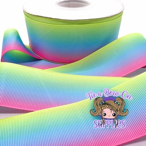 May include: A roll of colorful grosgrain ribbon with a gradient of pink, blue, green, and yellow. The ribbon is textured and has a vertical ribbed pattern. The image includes the text "Tie a Bow On SUPPLIES".
