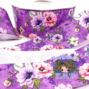 May include: Purple floral ribbon with a white ribbed underside. The ribbon features a repeating pattern of pink and purple anemone flowers with green leaves. The text "Tie a Bow On SUPPLIES" is visible on the ribbon.