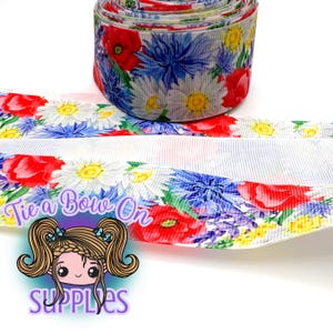May include: A roll of floral ribbon featuring red poppies, blue cornflowers, and yellow daisies on a white background. The ribbon is unrolled, revealing the same floral pattern. The text "Tie a Bow On" is displayed on the ribbon.
