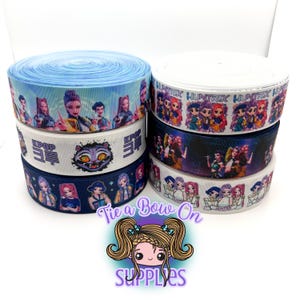 May include: Several spools of decorative ribbon featuring K-pop and cartoon character designs. The ribbons are in various colors, including blue, white, and navy, with printed images of stylized figures. The text "KPOP" and "HUNTRIX" are visible on some ribbons.