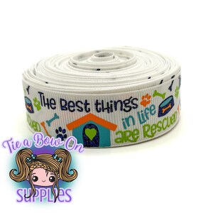Könnte beinhalten: Eine Rolle weißes Band mit dem Text "The best things in life are rescued" und Hunde-Motiven. Das Band zeigt ein Hundehäuschen, Pfotenabdrücke und einen Futternapf in Blau, Orange und Grün.