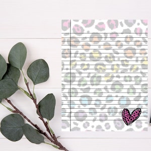 May include: A white sheet of paper with a black and white leopard print pattern. The paper has black lines across it and a pink heart drawn in the bottom right corner.