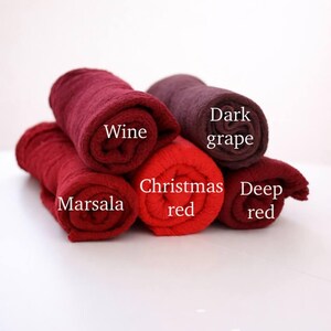 a collection of rolled towels in various colors, including red, wine, deep red, and dark grape, arranged on a white surface.