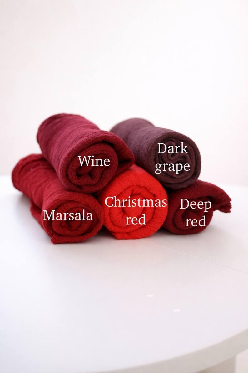 a collection of rolled towels in various colors, including red, wine, deep red, and dark grape, arranged on a white surface.