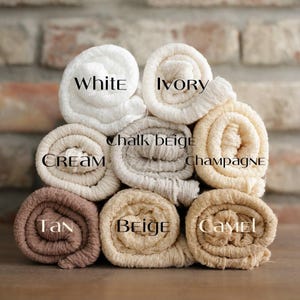 May include: A collection of rolled fabric in a range of neutral shades: white, ivory, cream, chalk beige, champagne, tan, beige, and camel. Each roll is labelled with its colour name in a decorative font.