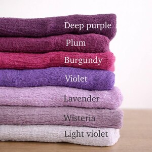 A stack of six towels in various shades of purple, including deep purple, plum, burgundy, violet, lavender, and light violet.