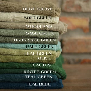 A stack of various colored towels, each labeled with a different color, including olive green, soft green, woodland, and teal blue.