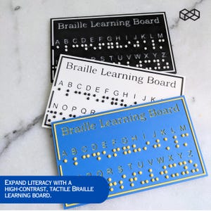 May include: Three Braille Learning Boards in black, white, and blue. Each board displays the alphabet in Braille, with raised dots for tactile learning. The blue board has gold lettering and a yellow border. The text reads "Braille Learning Board".