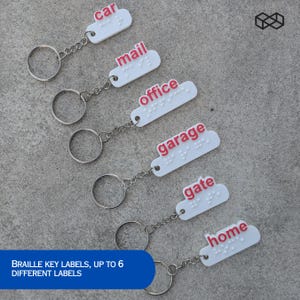 Peut inclure: Porte-clés blancs avec des étiquettes en texte rouge et en braille, indiquant "car", "mail", "office", "garage", "gate" et "home". Chaque étiquette en forme de nuage est attachée à une chaîne et un porte-clés argentés. Le texte "BRAILLE KEY LABELS, UP TO 6 DIFFERENT LABELS" est dans un rectangle bleu.