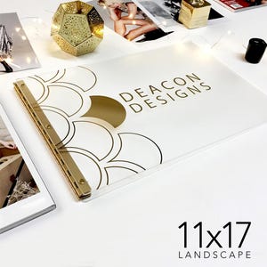 May include: A white, 11x17 inch landscape-oriented acrylic presentation folder with gold accents. The folder features a geometric pattern of overlapping circles and the text "DEACON DESIGNS" in gold lettering.