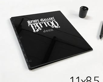 Puede incluir: Carpeta negra de tres anillos con un logotipo blanco que dice "Spirit Gallery Tattoo" y "John". La carpeta mide 28 cm por 21,5 cm.