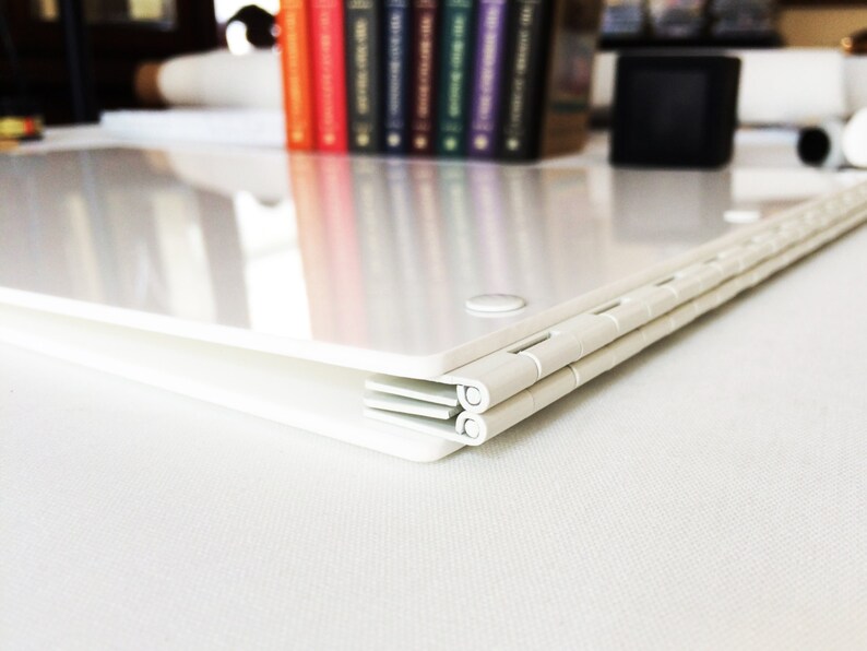 Puede incluir: Carpeta de pl&aacute;stico blanco con una bisagra de metal. La carpeta est&aacute; cerrada y se encuentra sobre una superficie blanca.