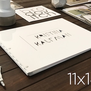 Puede incluir: &Aacute;lbum de fotos blanco con un t&iacute;tulo blanco recortado "Kristina Kaufmann" en la portada. El &aacute;lbum est&aacute; cerrado y sobre una superficie de madera. El texto "11x14" est&aacute; impreso en la superficie debajo del &aacute;lbum.