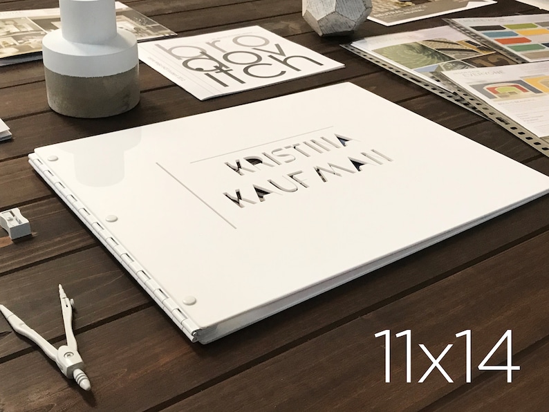 Puede incluir: &Aacute;lbum de fotos blanco con un t&iacute;tulo blanco recortado "Kristina Kaufmann" en la portada. El &aacute;lbum est&aacute; cerrado y sobre una superficie de madera. El texto "11x14" est&aacute; impreso en la superficie debajo del &aacute;lbum.