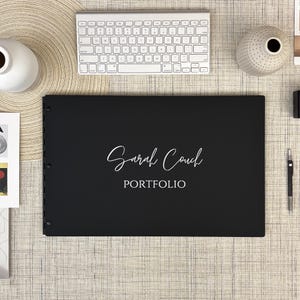 May include: Black portfolio binder with a white inscription that reads "Sarah Couch PORTFOLIO".