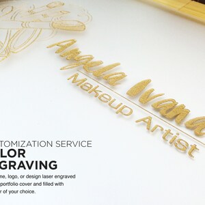 May include: A white background with gold lettering that reads "Angela Ivana Makeup Artist". The image also includes a gold outline of makeup brushes.