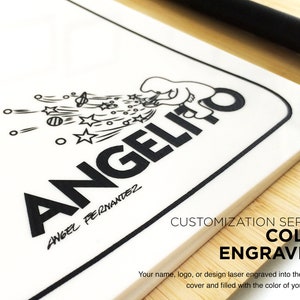 Puede incluir: Una cubierta de portafolio blanca con una ilustraci&oacute;n en blanco y negro de un personaje de dibujos animados con el texto "ANGELICO" y "ANGEL FERNANDEZ" debajo. El texto "CUSTOMIZATION SERVICE COLOR ENGRAVING" est&aacute; impreso debajo de la ilustraci&oacute;n. El texto "Your name, logo, or design laser engraved into the portfolio cover and filled with the color of your choice." est&aacute; impreso debajo del texto.