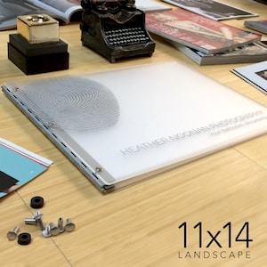 May include: A white, 11x14 inch, landscape photo album with a silver metal binding. The album cover has a fingerprint design and the text "HEATHER NOONAN PHOTOGRAPHY Your memories, documented."