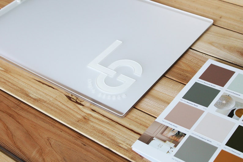 May include: A white acrylic sign with the letters "LG" embossed in white. The sign is on a wooden surface.