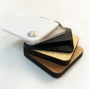 May include: A stack of four square-shaped pieces of material. The top piece is white, the second piece is clear, the third piece is black, and the bottom piece is a light brown wood.