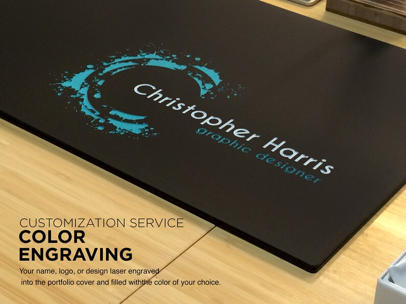 K&ouml;nnte beinhalten: Ein schwarzer Portfolio-Umschlag mit einem blauen und wei&szlig;en Logo, auf dem "Christopher Harris graphic designer" steht. Der Umschlag bietet einen "Farbgravur"-Service, bei dem Sie Ihren Namen, Ihr Logo oder Ihr Design lasergravieren und mit der Farbe Ihrer Wahl f&uuml;llen lassen k&ouml;nnen.