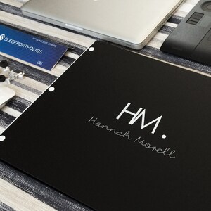 K&ouml;nnte beinhalten: Ein schwarzes Portfolio mit wei&szlig;en Buchstaben, auf dem "HM. Hannah Morell" steht.