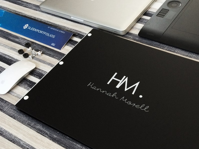 K&ouml;nnte beinhalten: Ein schwarzes Portfolio mit wei&szlig;en Buchstaben, auf dem "HM. Hannah Morell" steht.