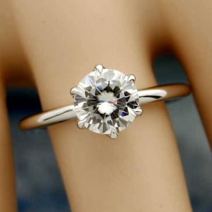 May include: A solitaire engagement ring featuring a large, round-cut diamond set in a silver band. The diamond sparkles brightly, showcasing its facets. The ring is a classic design, perfect for proposals and special occasions.