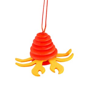 May include: A red and yellow wooden toy crab with a layered body and a red string hanging from the top.