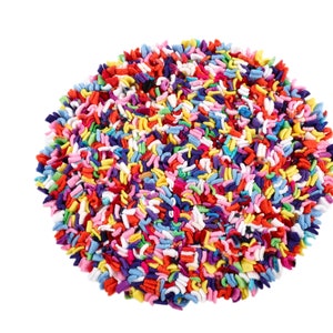 May include: A round, colourful rug made of fabric scraps. The rug is made up of many different colours, including red, orange, yellow, green, blue, purple, and white.